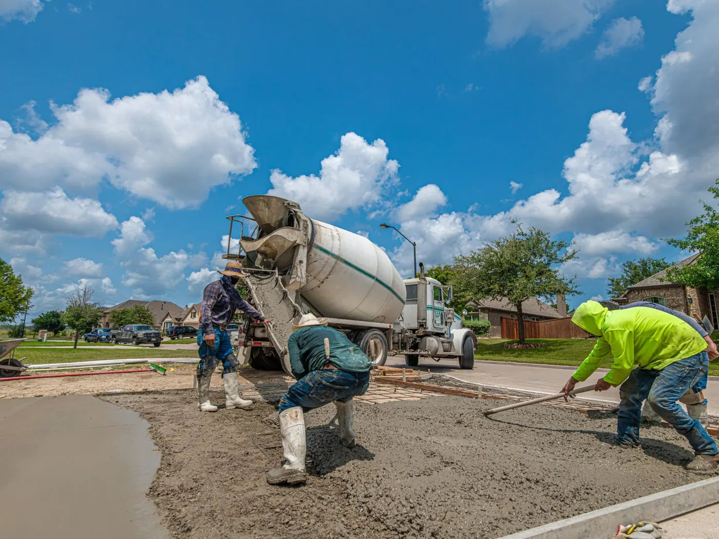 Crew screeding fresh concrete beside a mixer truck on a driveway pour