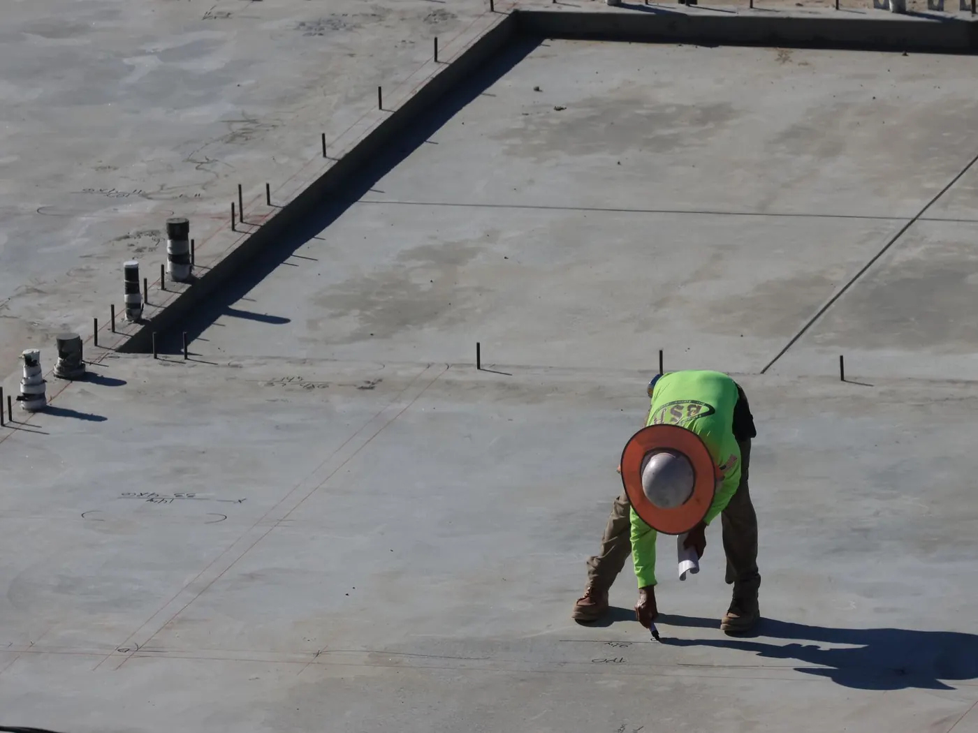 Worker finishing a formed concrete slab with anchor bolts set along the edge