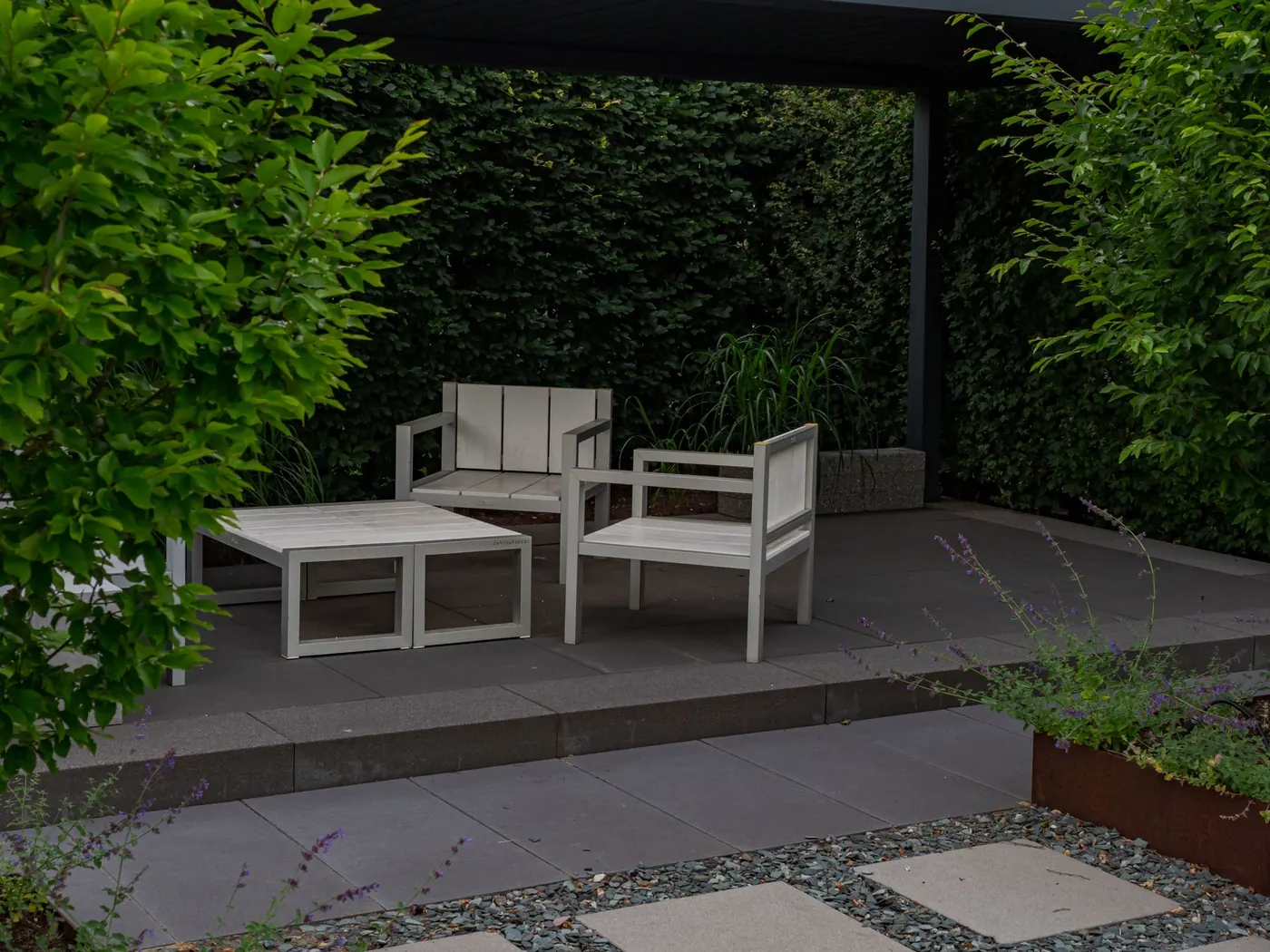 Outdoor lounge furniture on a paved patio next to a clipped hedge